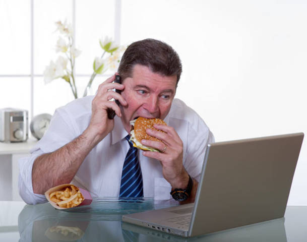 A man eating a burger while operating a laptop